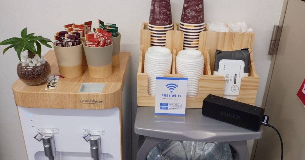 コスモウォーターのサーバーとスティックコーヒーや紙コップおよび無料Wi-Fiの案内が置かれたドリンクコーナー