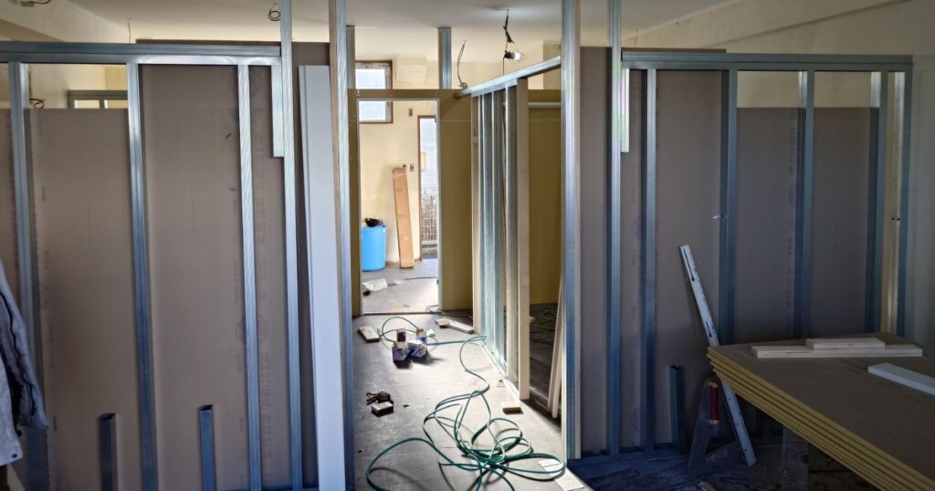 部屋の中に金属の骨組みを立てて壁の板を張っている内装工事の様子