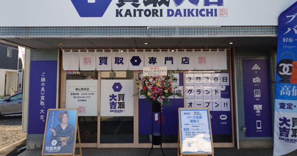 2月20日開店の貼り紙とお祝いの花が飾られた買取大吉狭山笹井店の外観